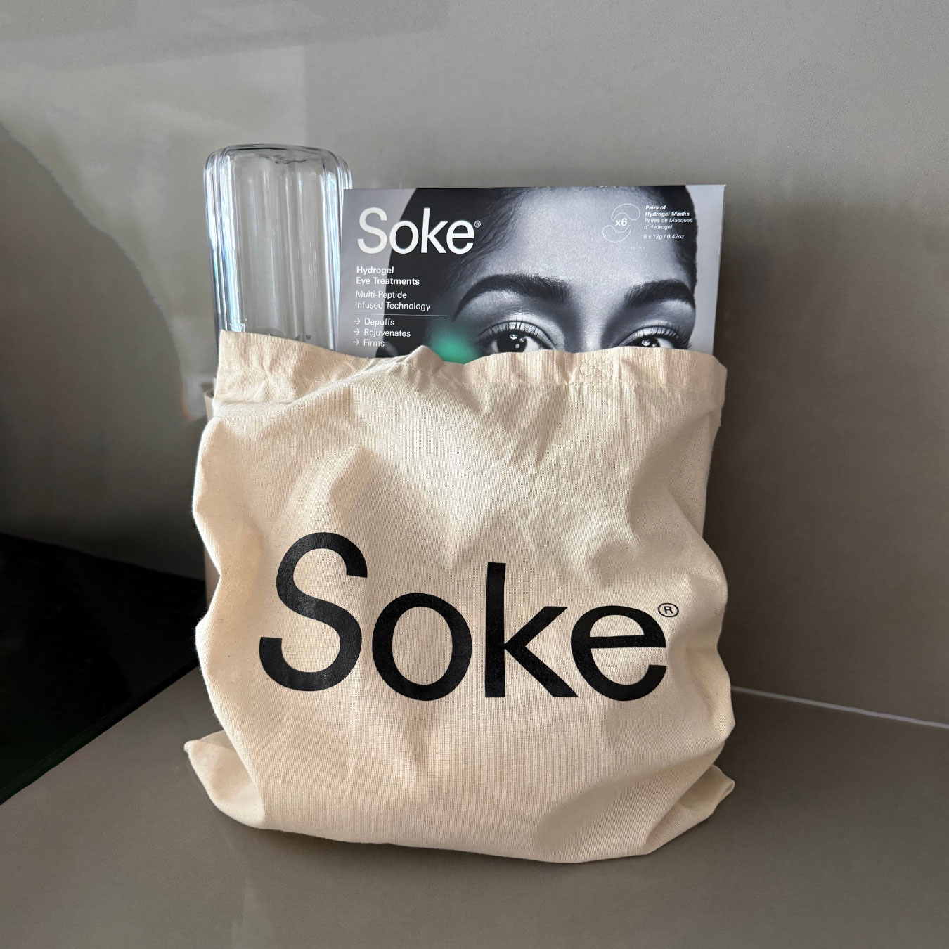Soke tote bag styled with Soke Eye Treatments box and glass water bottle on counter, lifestyle product image.