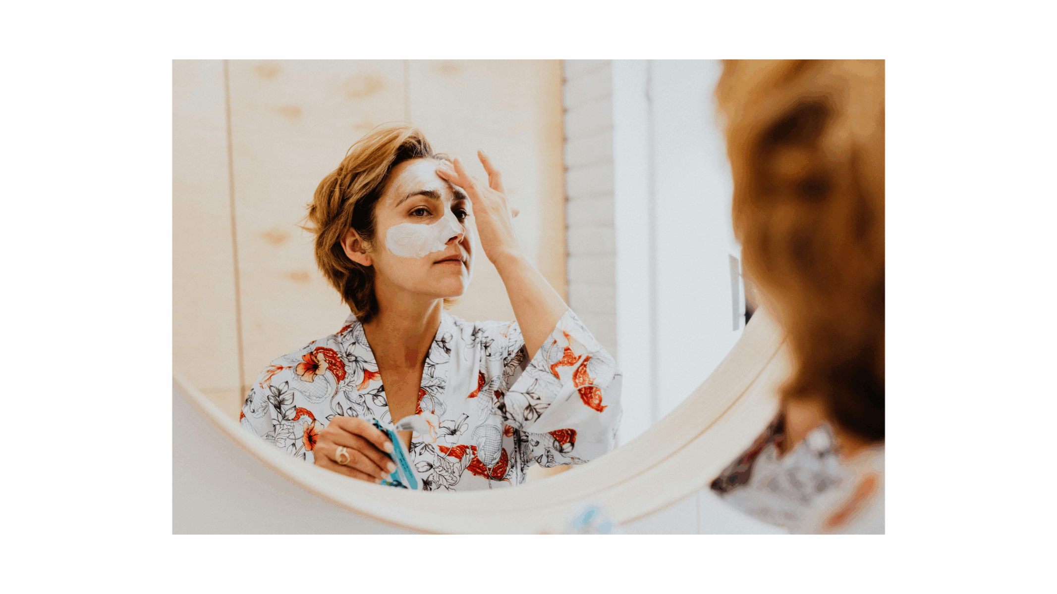 Woman applying skincare mask in front of mirror.