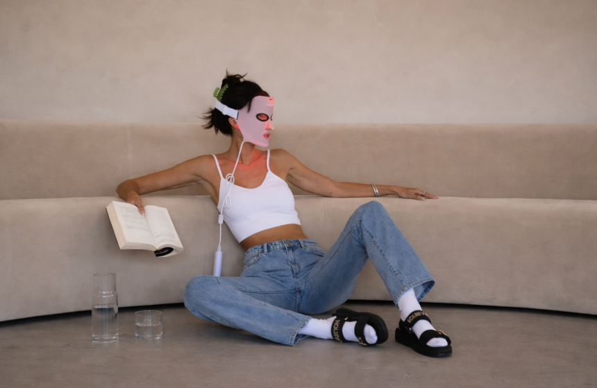 Woman relaxing on a sofa wearing a light therapy face mask during a self-care skincare ritual