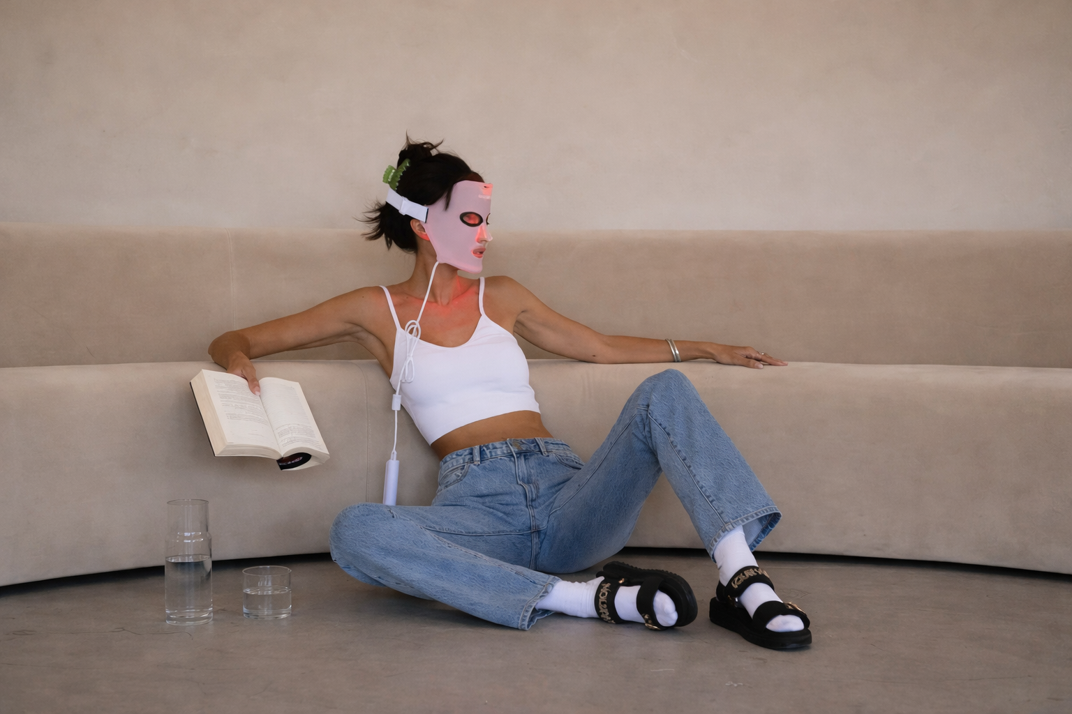 Woman relaxing on a sofa wearing a light therapy face mask during a self-care skincare ritual